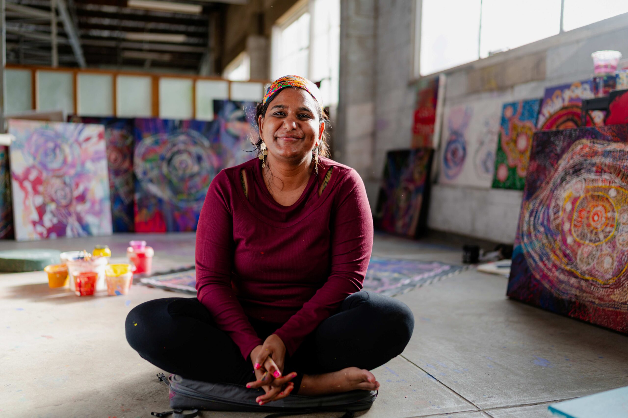 Lisa Kahn sitting on the floor in an art studio, smiling to camera